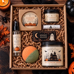 May include: A gift box containing a Pumpkin Spice soap, Harmony body butter, a lip balm with an eye symbol, a Spooky Season bar, a Pumpkin Spice body spray, a two-toned orange and green bath bomb, and a Halloween Night soy wax candle.
