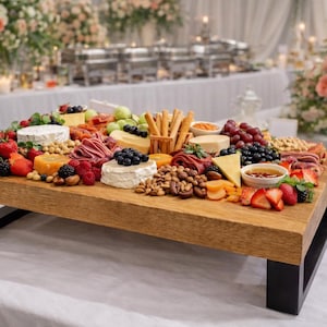 May include: A rectangular wooden serving board with a thick natural grain top and black metal U-shaped legs. The board is arranged with an assortment of cheeses, cured meats, fresh berries, grapes, nuts, breadsticks, and a small bowl of honey.