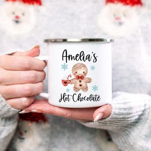 Puede incluir: Taza de esmalte blanco con una ilustraci&oacute;n de un hombre de jengibre y el texto "Amelia's Hot Chocolate".
