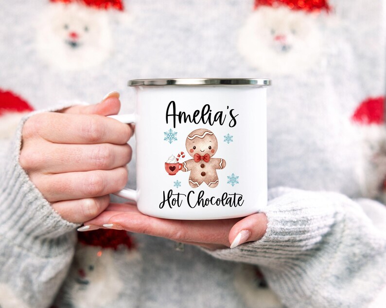 Puede incluir: Taza de esmalte blanco con una ilustraci&oacute;n de un hombre de jengibre y el texto "Amelia's Hot Chocolate".