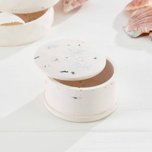 May include: White ceramic trinket box with a speckled design and a lid. The lid has a small hole in the centre.