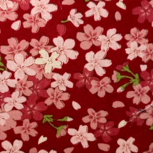 Puede incluir: Tela roja con un patr&oacute;n repetido de flores de cerezo rosas y blancas. La tela tiene una textura sutil.