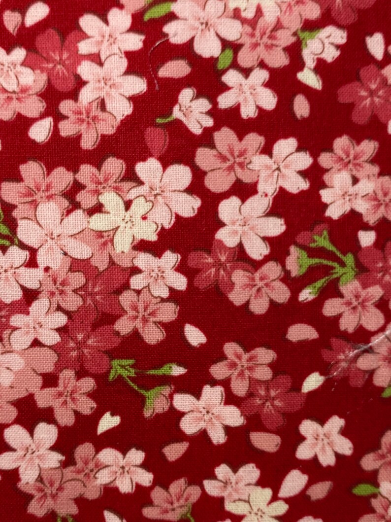 Puede incluir: Tela roja con un patr&oacute;n repetido de flores de cerezo rosas y blancas. La tela tiene una textura sutil.