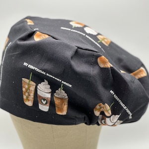 May include: Black scrub hat with a repeating pattern of coffee cups with whipped cream and the text "My Emotional Support Drink".