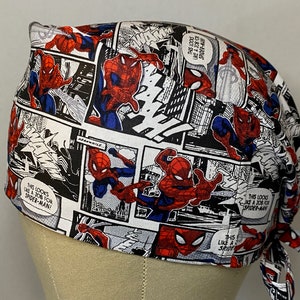 Pu&ograve; includere: Un berretto chirurgico bianco, rosso e nero con un design a fumetti con Spiderman. Il berretto ha lacci sul retro e il testo "This looks like a job for Spiderman!" &egrave; stampato sul berretto.