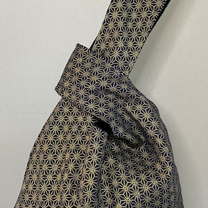 May include: A navy blue tote bag with a gold geometric pattern. The bag has a knotted handle.