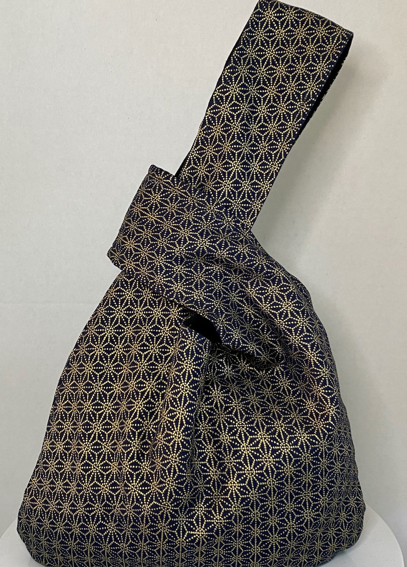 May include: A navy blue tote bag with a gold geometric pattern. The bag has a knotted handle.