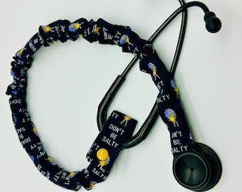May include: Black stethoscope with a blue and yellow patterned fabric cover. The fabric has the text "Don't Be Salty" repeated on it.