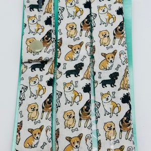 May include: Three white fabric strips with a repeating pattern of various dog breeds in black, brown, and white. The fabric has a light green border and a white background with small bone shapes.