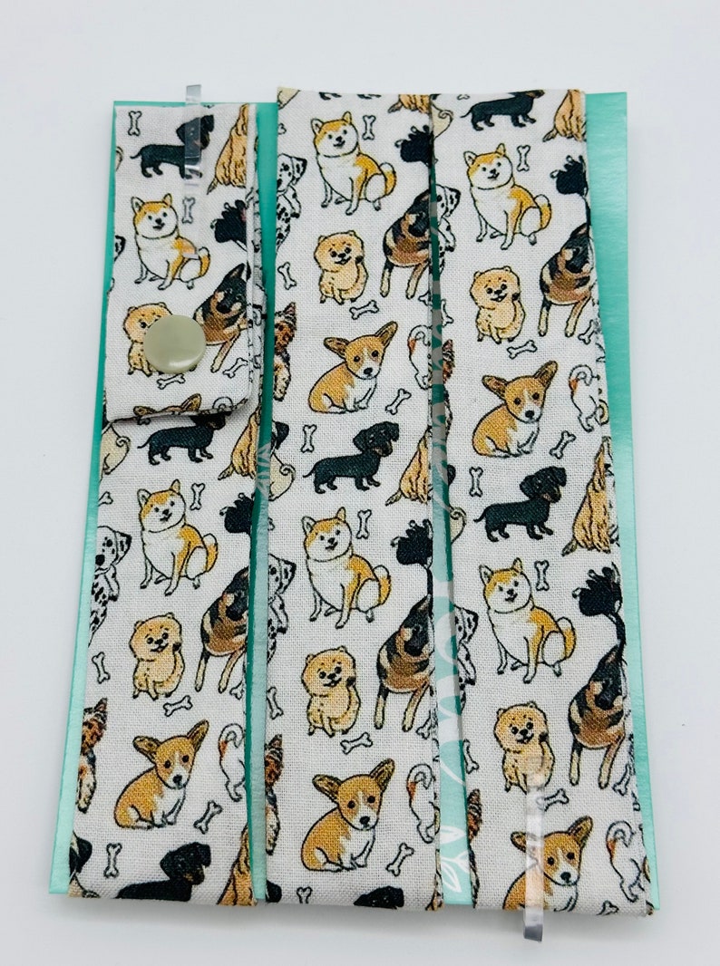 May include: Three white fabric strips with a repeating pattern of various dog breeds in black, brown, and white. The fabric has a light green border and a white background with small bone shapes.