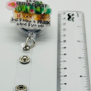 Peut inclure: Un porte-badge &agrave; th&egrave;me cactus blanc et vert avec le texte "Je ne suis pas un expert en cactus mais je connais un piquant quand j'en vois un".