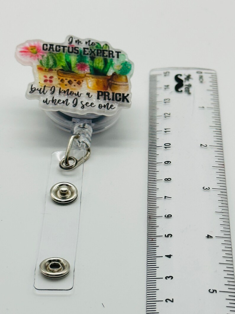 Peut inclure: Un porte-badge &agrave; th&egrave;me cactus blanc et vert avec le texte "Je ne suis pas un expert en cactus mais je connais un piquant quand j'en vois un".