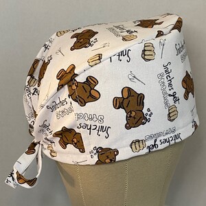 May include: White scrub hat with a brown teddy bear print and the text "Stitches get stitches".