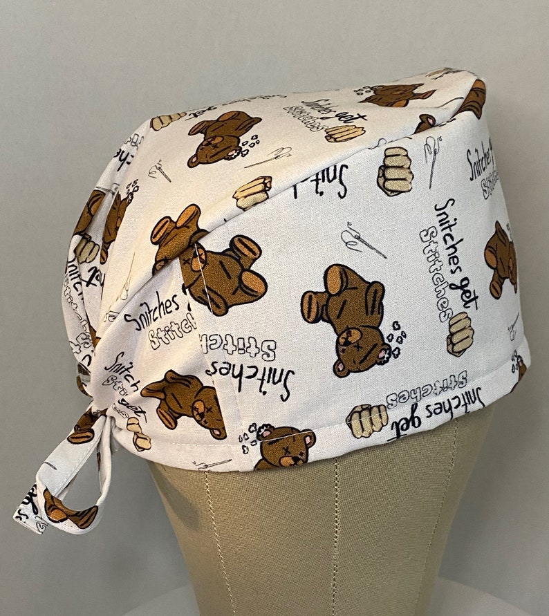 May include: White scrub hat with a brown teddy bear print and the text "Stitches get stitches".