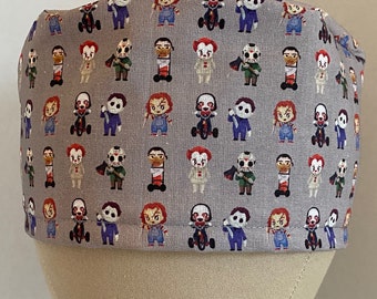 May include: A gray scrub hat with a repeating pattern of horror movie characters. The characters include Pennywise the clown, Jason Voorhees, Freddy Krueger, and Michael Myers.