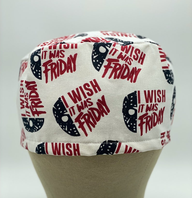 K&ouml;nnte beinhalten: Wei&szlig;e Stoff-Scrub-M&uuml;tze mit einem sich wiederholenden Muster aus schwarzen und wei&szlig;en Hockeymasken und dem Text "I Wish It Was Friday" in Rot.