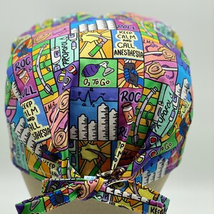 May include: A colourful surgical scrub hat with a cartoon-style design featuring medical equipment and the text "Keep Calm and Call Anesthesia".