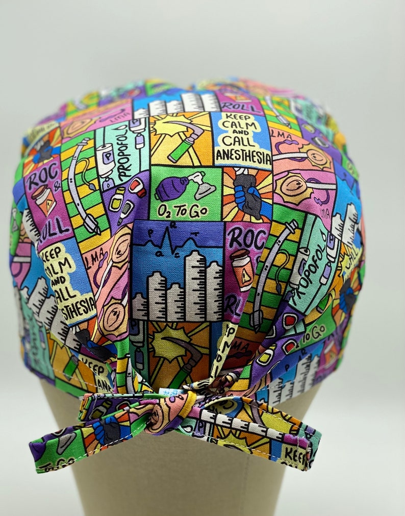 May include: A colourful surgical scrub hat with a cartoon-style design featuring medical equipment and the text "Keep Calm and Call Anesthesia".