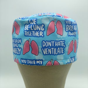 May include: Blue and pink patterned scrub hat with the text "We Be-Lung Together", "Don't Hate, Ventilate", "You Take My Breath Away" and a pink lung graphic.