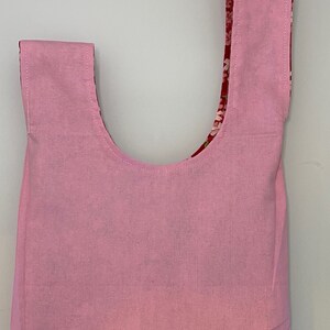 Puede incluir: Una bolsa de mano rosa con forro de estampado floral. La bolsa tiene una abertura ancha y dos asas largas.
