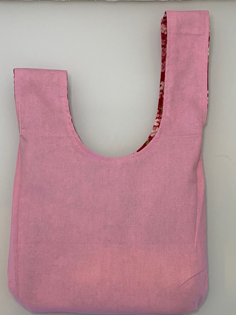 Puede incluir: Una bolsa de mano rosa con forro de estampado floral. La bolsa tiene una abertura ancha y dos asas largas.