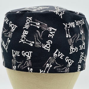 May include: Black surgical scrub cap with a repeating pattern of white skeletons and the text "I've Got Your Back". The cap is designed to cover the hair during medical procedures.