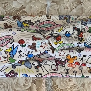 May include: White fabric headband featuring a colourful print of Disney characters, including Mickey Mouse, Minnie Mouse, Tinkerbell, and Chip and Dale. The print also includes the words "Walt Disney World" and "Disneyland".