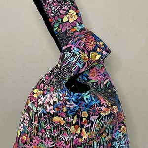 May include: A black tote bag with a floral print featuring a variety of colorful flowers on a black background. The bag has a knotted handle.