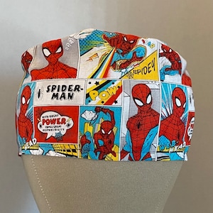 May include: A white scrub hat with a comic book pattern featuring Spider-Man. The hat has a red, blue, and yellow design with the words "Spider-Man" and "With great power comes great responsibility".