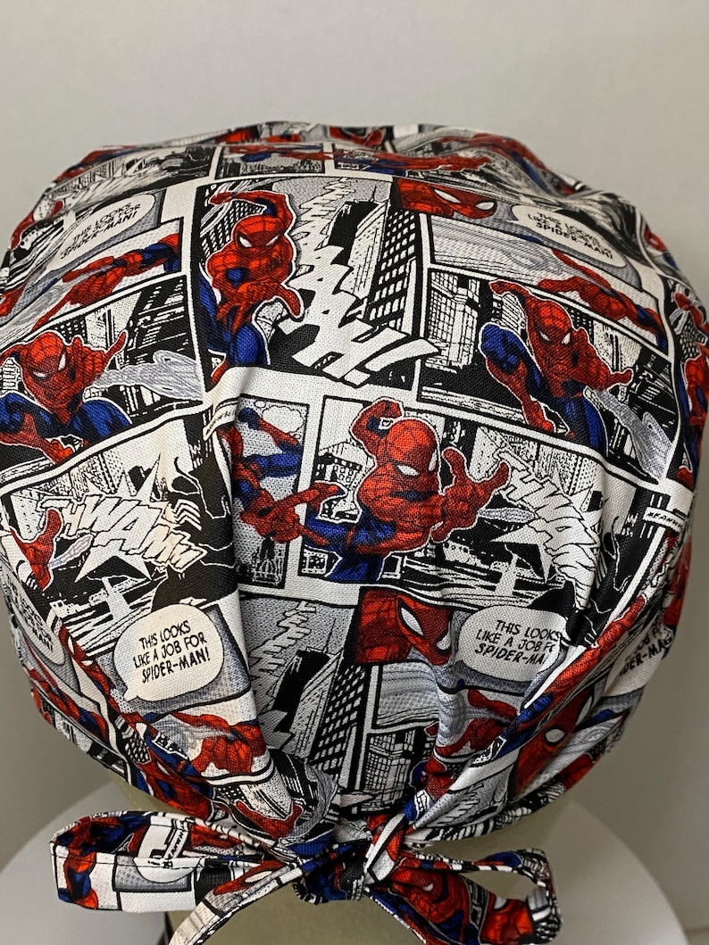 Pu&ograve; includere: Un berretto chirurgico in tessuto bianco, rosso e blu con un motivo a fumetti con Spider-Man. Il berretto ha un laccio sul retro. Il testo sul berretto recita "This looks like a job for Spider-Man!"
