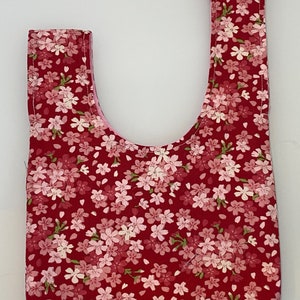 Puede incluir: Una bolsa de tela roja con un estampado floral rosa. La bolsa tiene una sola correa y una abertura ancha.