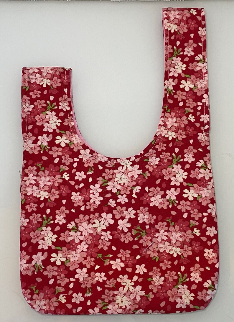 Puede incluir: Una bolsa de tela roja con un estampado floral rosa. La bolsa tiene una sola correa y una abertura ancha.