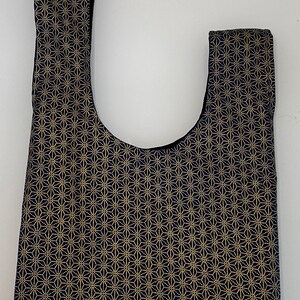 May include: A black and gold tote bag with a geometric pattern. The bag has a wide, flat bottom and two short straps.