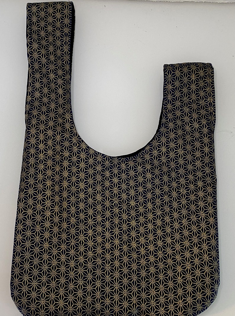 May include: A black and gold tote bag with a geometric pattern. The bag has a wide, flat bottom and two short straps.