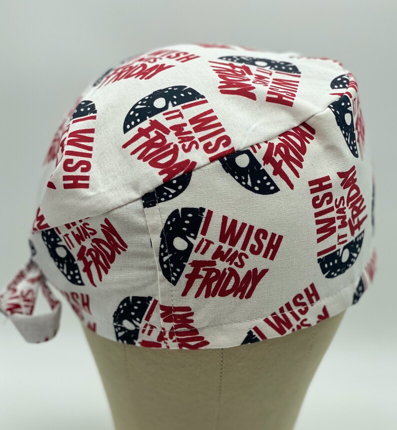 K&ouml;nnte beinhalten: Eine wei&szlig;e OP-M&uuml;tze mit einem sich wiederholenden Muster aus schwarzen und wei&szlig;en Hockeymasken und dem Text "I Wish It Was Friday" in Rot.
