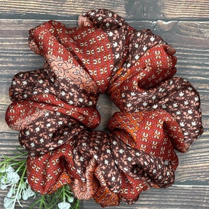 May include: A brown, orange, and pink patterned scrunchie made of fabric. The scrunchie is folded and tied into a circle shape.