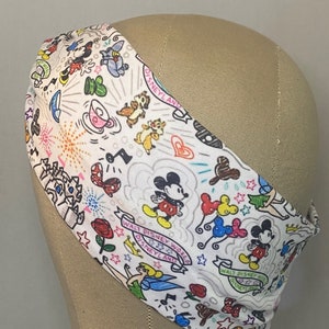 May include: White headband with a colourful print of Mickey Mouse and other Disney characters, including Tinkerbell, Chip and Dale, and the text "Walt Disney World Disneyland".