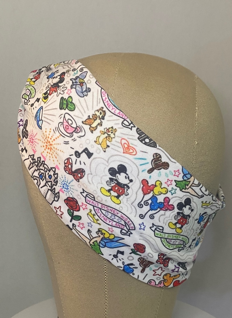 May include: White headband with a colourful print of Mickey Mouse and other Disney characters, including Tinkerbell, Chip and Dale, and the text "Walt Disney World Disneyland".