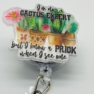 Peut inclure: Un porte-badge en paillettes blanches avec un motif de cactus et le texte "Je ne suis pas un expert en cactus mais je sais reconna&icirc;tre un piquant quand j'en vois un".