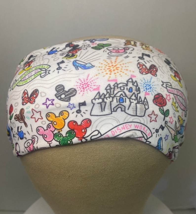 May include: White headband with a colourful doodle pattern featuring Mickey Mouse, Minnie Mouse, Cinderella's glass slipper, fireworks, and the text "Walt Disney World".