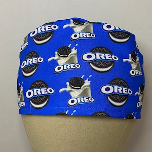 May include: Blue scrub hat with a repeating pattern of Oreo cookies and milk splashes. The text "OREO" is printed on the hat.