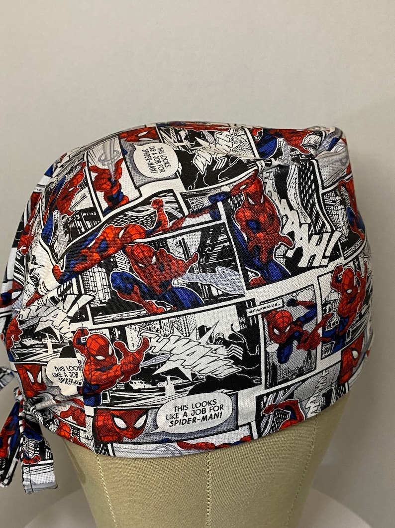 Pu&ograve; includere: Un berretto chirurgico bianco, rosso e blu con un motivo a fumetti con Spider-Man. Il testo sul berretto recita "This looks like a job for Spider-Man!"