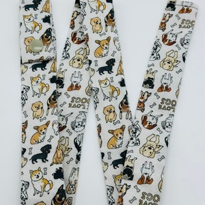 May include: White fabric lanyard with a repeating pattern of dogs and bones. The lanyard has a button closure and the text "LOVE DOGS" is repeated throughout the pattern.