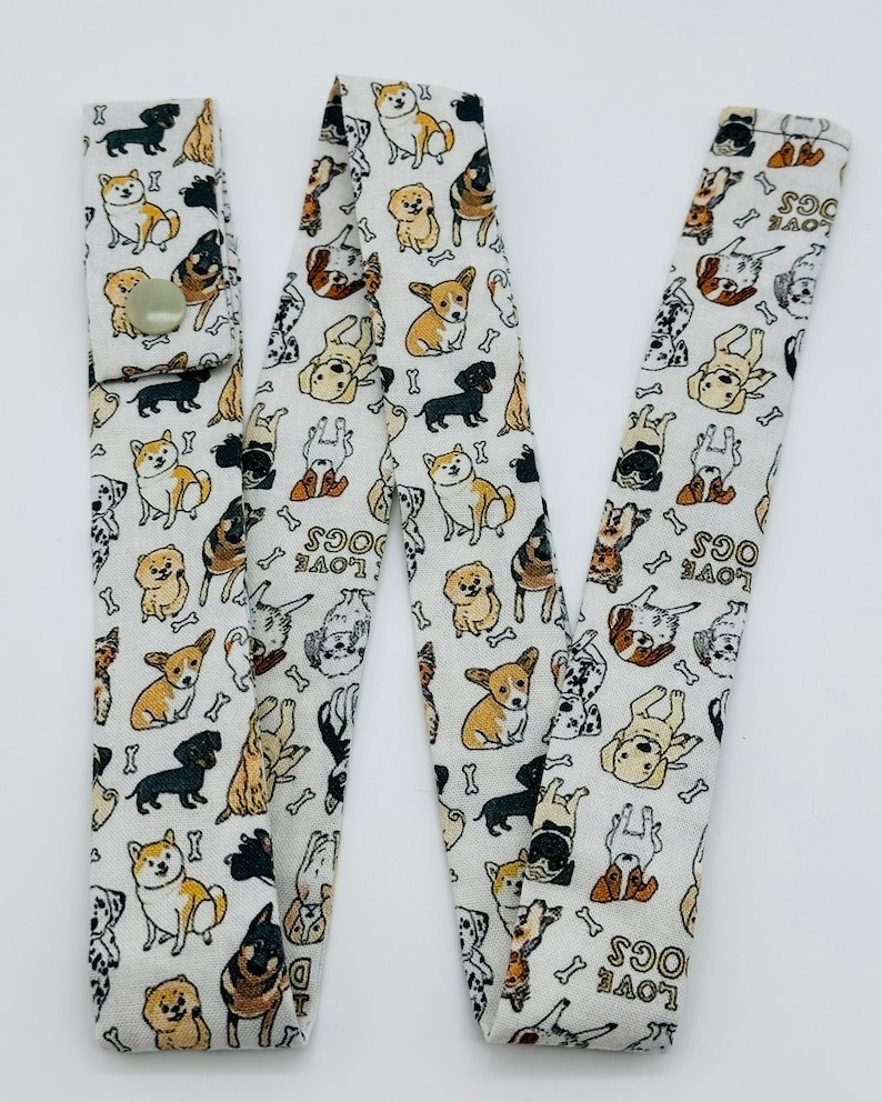 May include: White fabric lanyard with a repeating pattern of dogs and bones. The lanyard has a button closure and the text "LOVE DOGS" is repeated throughout the pattern.