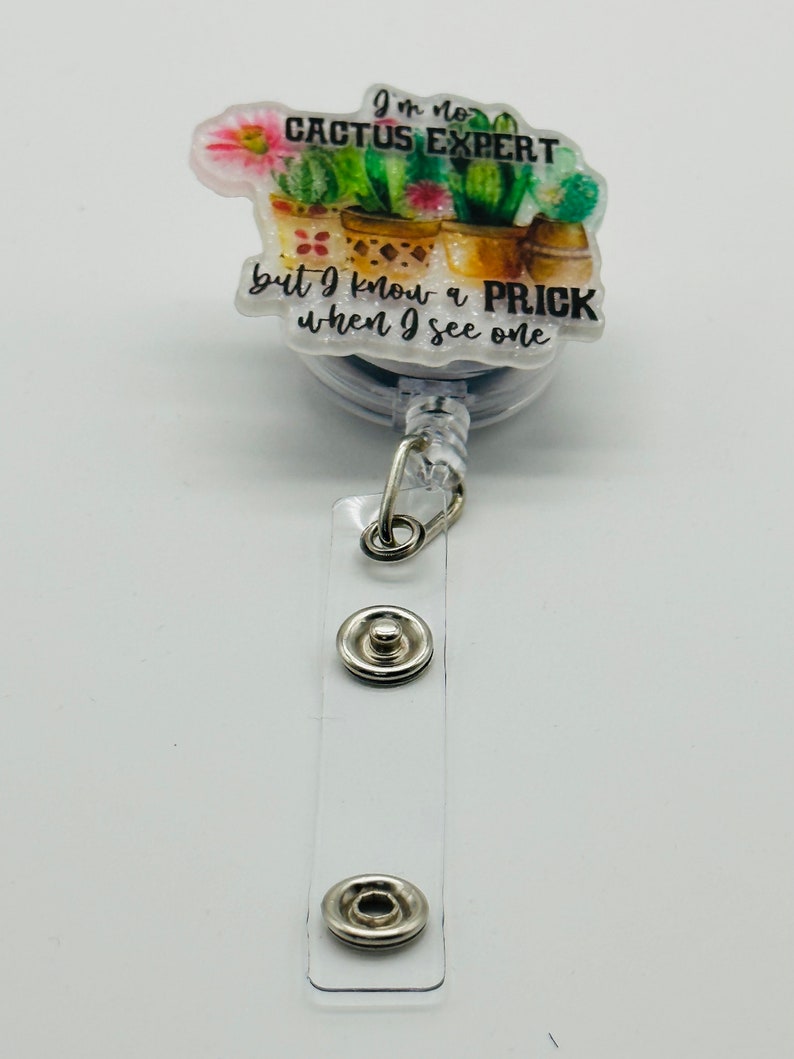 Peut inclure: Un porte-badge r&eacute;tractable &agrave; th&egrave;me cactus blanc et vert avec le texte "Je ne suis pas un expert en cactus mais je sais reconna&icirc;tre un piquant quand j'en vois un".