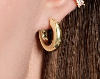 May include: A gold-toned hoop earring and a gold-toned ear cuff featuring a row of clear, rectangular-cut stones. The hoop is smooth and polished, while the ear cuff is set with multiple sparkling stones along its outer edge.