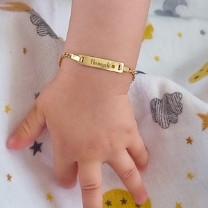 A baby's wrist with a personalized gold ID bracelet engraved with the name 'Hannah'.