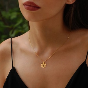 Gold pentagram necklace displayed on the neck of a person with subtle makeup and a black strap top, highlighting the pendant's design.