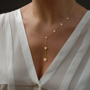 Elegant gold Y necklace with multiple heart-shaped pendants resting on the neckline of a white blouse.