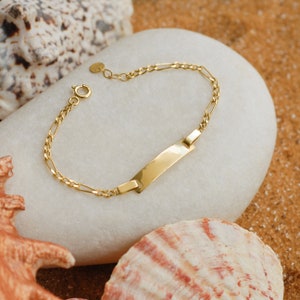 Gold ID bracelet on a white stone surface, set against a beach background with starfish and shells.